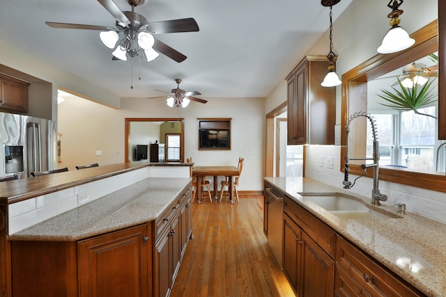 kitchen with sink, hardwood / wood-style floors, light stone countertops, decorative light fixtures, and stainless steel dishwasher