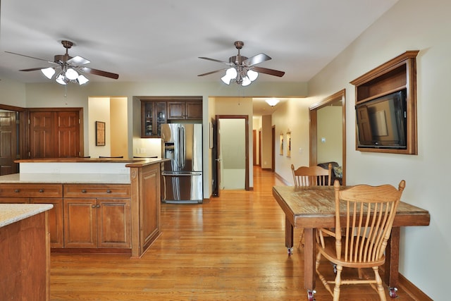 kitchen with stainless steel refrigerator with ice dispenser, light stone counters, ceiling fan, and light wood-type flooring