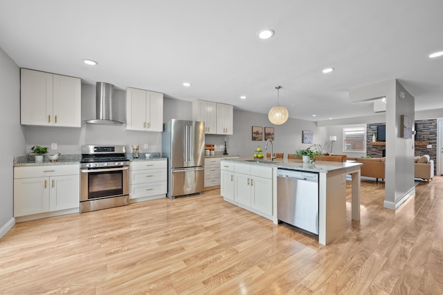 kitchen with wall chimney exhaust hood, stainless steel appliances, sink, decorative light fixtures, and white cabinetry