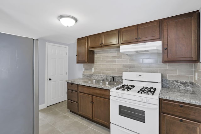 kitchen with sink, decorative backsplash, light tile patterned floors, white gas stove, and dark brown cabinets