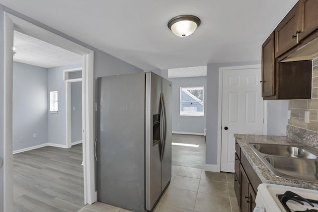 kitchen featuring stove, sink, stainless steel refrigerator with ice dispenser, light tile patterned flooring, and dark brown cabinetry