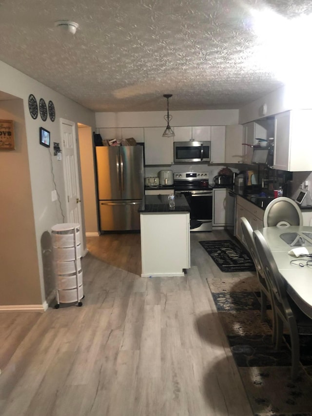 kitchen featuring white cabinetry, decorative light fixtures, light hardwood / wood-style flooring, a textured ceiling, and appliances with stainless steel finishes