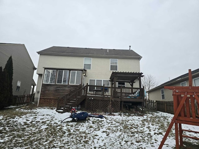 snow covered back of property with a deck and a pergola