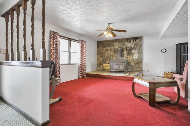 living room featuring ceiling fan, a wood stove, a textured ceiling, and carpet flooring