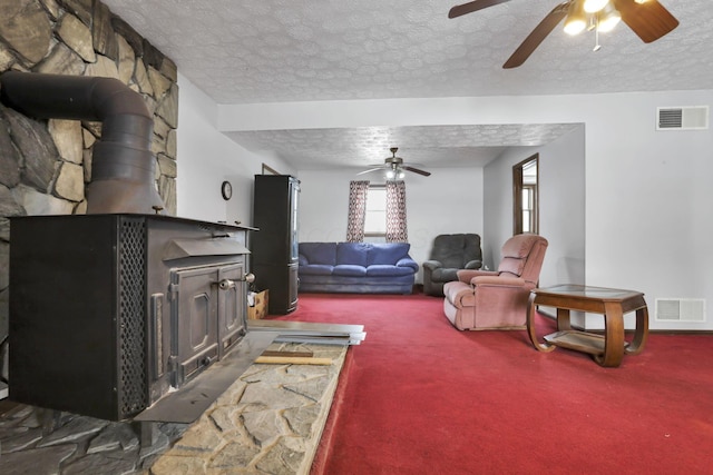 carpeted living room featuring ceiling fan, a wood stove, and a textured ceiling