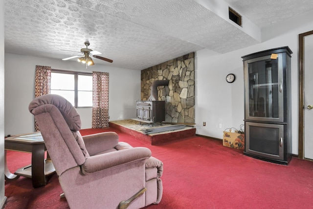 living room with carpet flooring, ceiling fan, a textured ceiling, and a wood stove