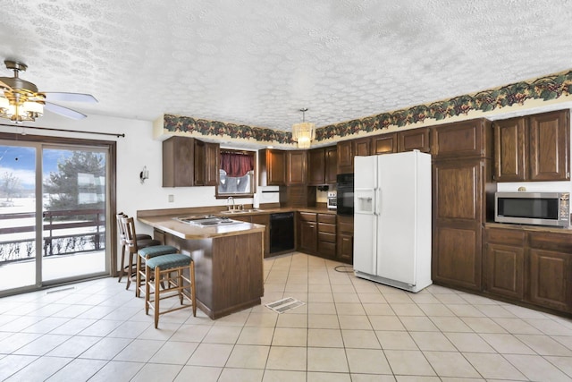 kitchen with pendant lighting, light tile patterned floors, dark brown cabinetry, black appliances, and a kitchen bar