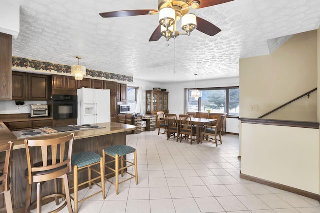 kitchen featuring a breakfast bar, pendant lighting, oven, white refrigerator with ice dispenser, and dark brown cabinetry