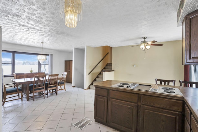 kitchen featuring light tile patterned floors, ceiling fan with notable chandelier, dark brown cabinetry, a textured ceiling, and decorative light fixtures