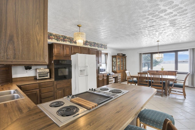 kitchen featuring a notable chandelier, white refrigerator with ice dispenser, pendant lighting, and black oven