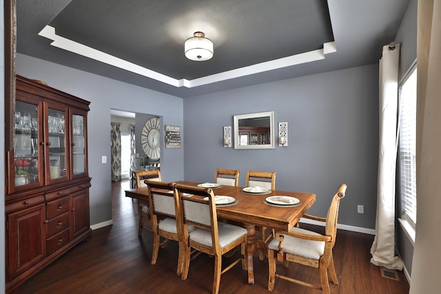 dining space with a raised ceiling and dark wood-type flooring