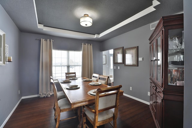 dining room with a textured ceiling, dark hardwood / wood-style flooring, and a raised ceiling