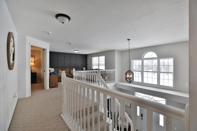 hall featuring a textured ceiling, a chandelier, and light carpet