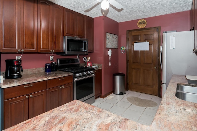 kitchen with ceiling fan, light stone countertops, stainless steel appliances, a textured ceiling, and light tile patterned floors