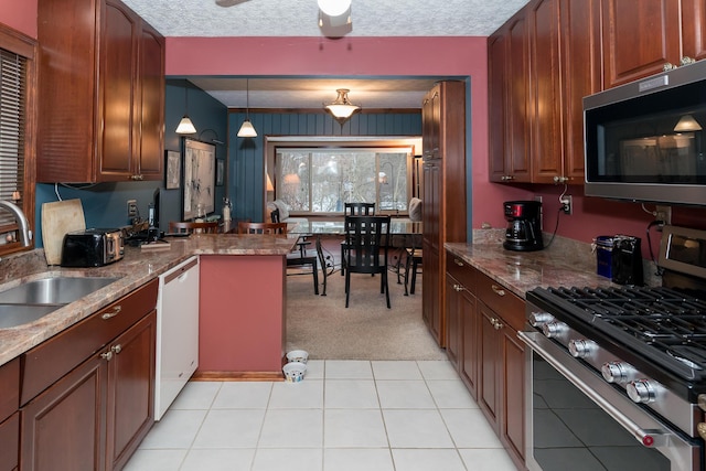 kitchen featuring appliances with stainless steel finishes, light carpet, dark stone counters, sink, and hanging light fixtures