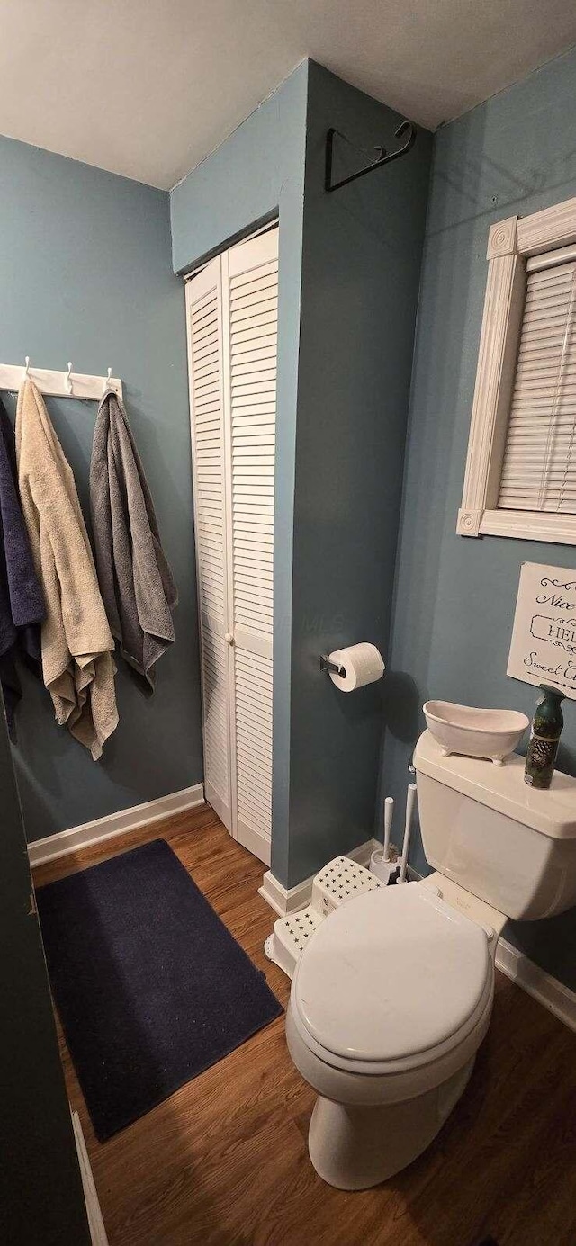 bathroom with a closet, baseboards, toilet, and wood finished floors