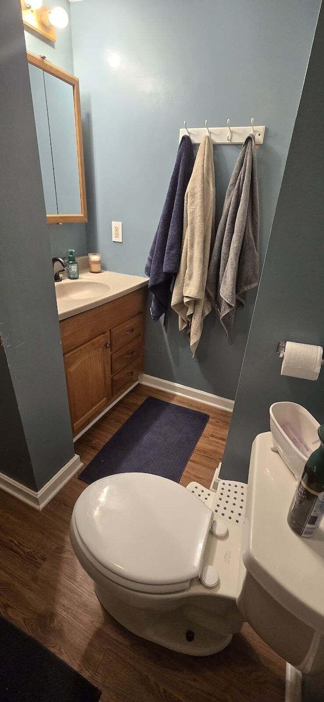 half bathroom with vanity, wood finished floors, toilet, and baseboards