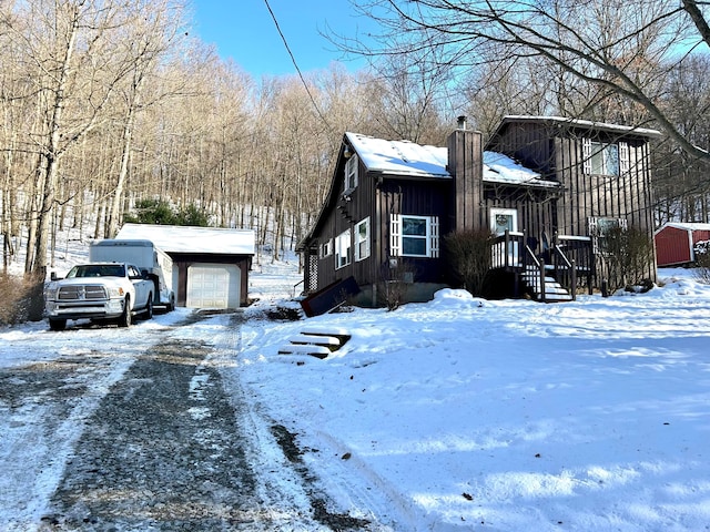 view of snow covered exterior with a garage, a chimney, and an outdoor structure