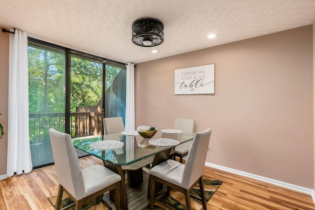 dining room with a wall of windows, a textured ceiling, and light hardwood / wood-style flooring