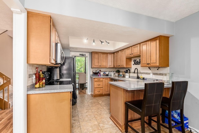 kitchen featuring kitchen peninsula, a textured ceiling, a tray ceiling, sink, and a breakfast bar area