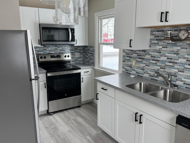 kitchen featuring decorative backsplash, sink, light wood-type flooring, stainless steel appliances, and white cabinets