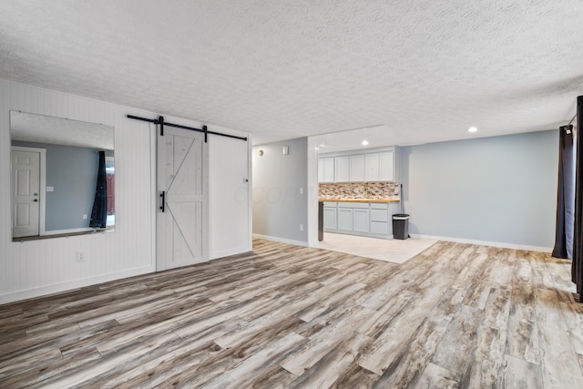 unfurnished living room featuring a barn door, a textured ceiling, and light hardwood / wood-style flooring