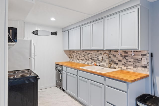 kitchen with sink, butcher block counters, white refrigerator, washer / clothes dryer, and black range with electric cooktop