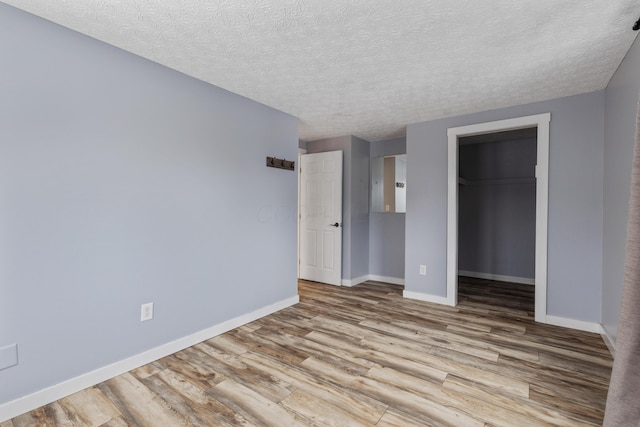 unfurnished bedroom with a walk in closet, light hardwood / wood-style flooring, a closet, and a textured ceiling