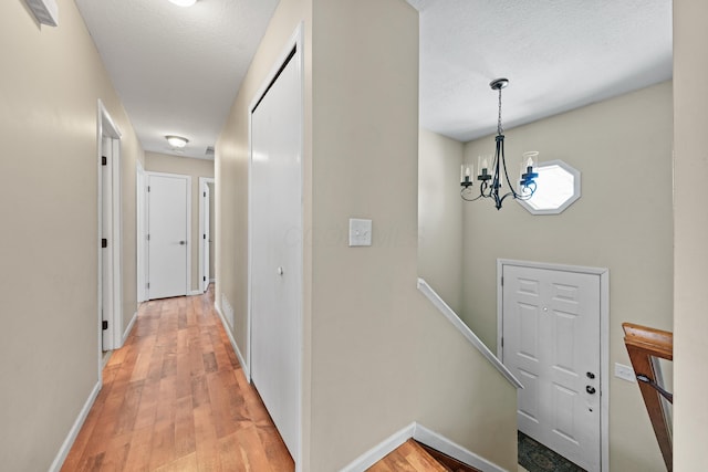 corridor with hardwood / wood-style floors, an inviting chandelier, and a textured ceiling