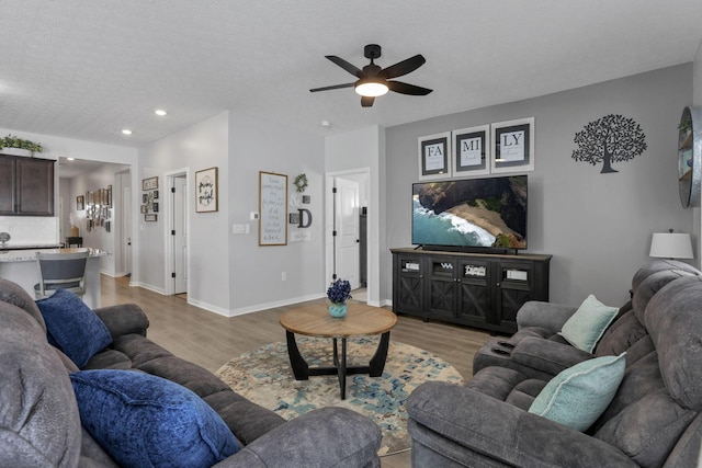 living room with a textured ceiling, light wood-type flooring, and ceiling fan