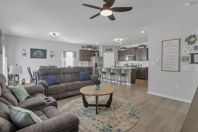 living room with ceiling fan, light hardwood / wood-style flooring, a textured ceiling, and sink