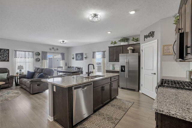 kitchen with appliances with stainless steel finishes, dark brown cabinets, a textured ceiling, sink, and a center island with sink