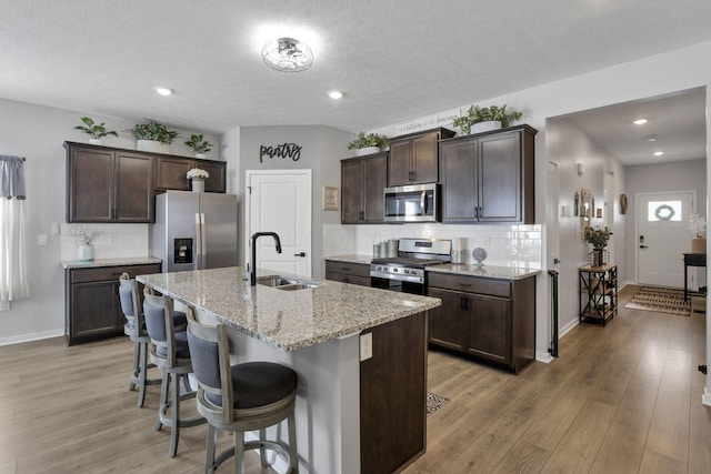 kitchen with dark brown cabinetry, a kitchen island with sink, sink, and stainless steel appliances