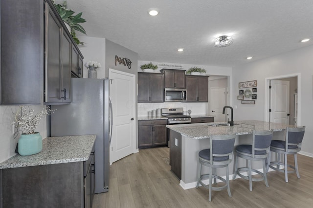 kitchen with a center island with sink, sink, light stone countertops, appliances with stainless steel finishes, and tasteful backsplash