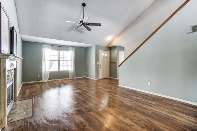 unfurnished living room featuring dark wood-type flooring, lofted ceiling, a textured ceiling, a tile fireplace, and ceiling fan