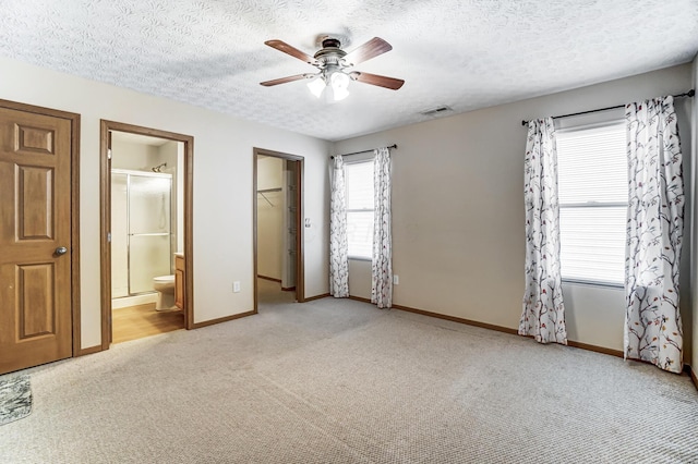 unfurnished bedroom featuring ensuite bathroom, a spacious closet, light colored carpet, and a textured ceiling