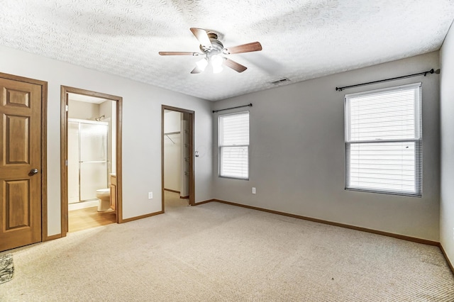 unfurnished bedroom featuring ensuite bath, a walk in closet, light carpet, a textured ceiling, and a closet