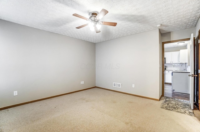 spare room featuring sink, light colored carpet, a textured ceiling, and ceiling fan