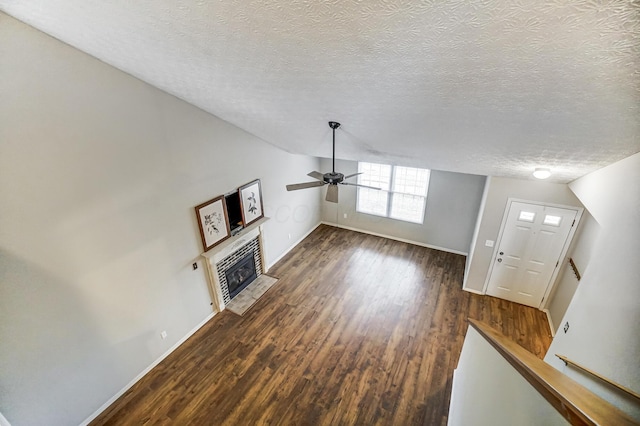 unfurnished living room featuring a tiled fireplace, vaulted ceiling, dark wood-type flooring, and a textured ceiling