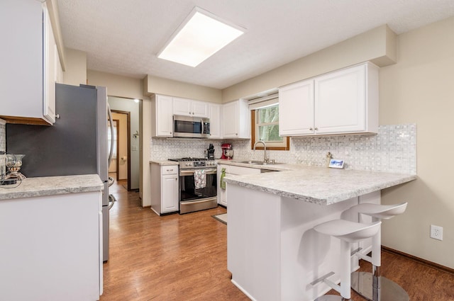 kitchen featuring stainless steel appliances, white cabinetry, sink, and a kitchen bar