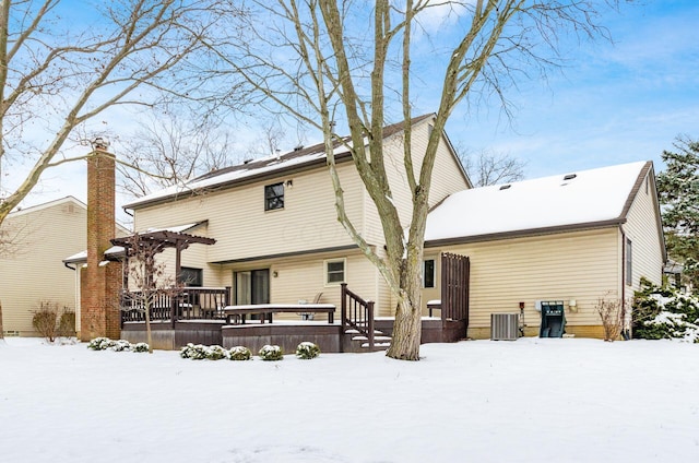 snow covered back of property featuring central AC, a wooden deck, and a pergola