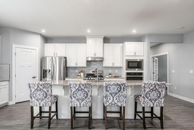 kitchen with white cabinetry, appliances with stainless steel finishes, a kitchen island with sink, and decorative backsplash