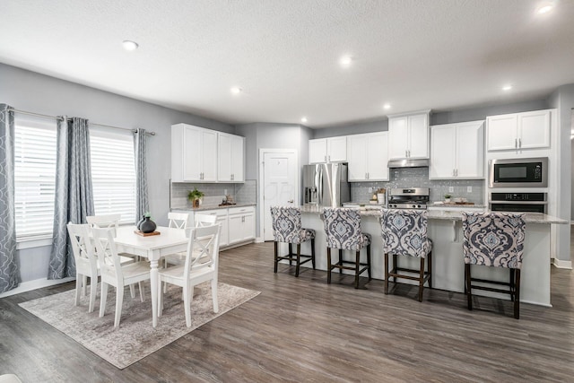 kitchen with white cabinetry, a center island with sink, stainless steel appliances, dark hardwood / wood-style floors, and a kitchen bar