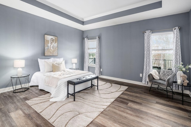 bedroom with multiple windows, dark hardwood / wood-style floors, ornamental molding, and a raised ceiling