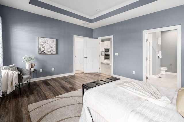 bedroom featuring hardwood / wood-style floors, ensuite bath, and a tray ceiling