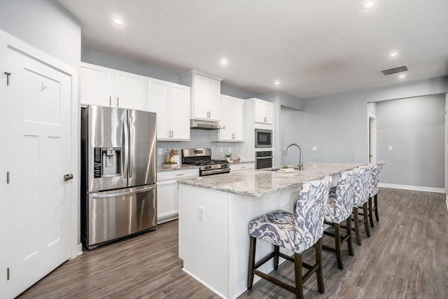 kitchen with appliances with stainless steel finishes, white cabinetry, a center island with sink, dark hardwood / wood-style floors, and a kitchen bar