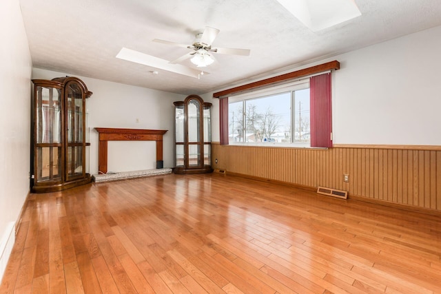 unfurnished living room with ceiling fan, a skylight, and light hardwood / wood-style floors