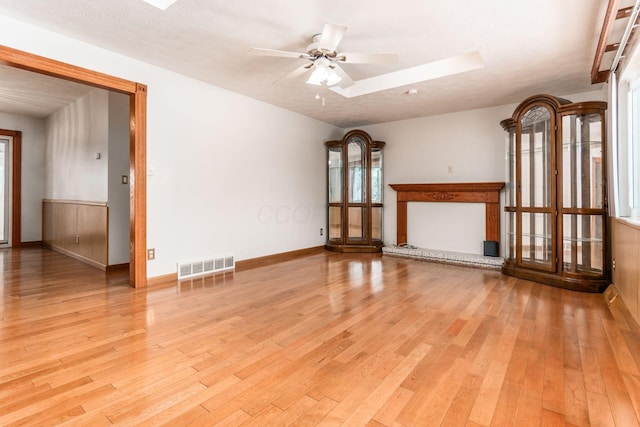 unfurnished living room with a textured ceiling, ceiling fan, light hardwood / wood-style floors, and a skylight