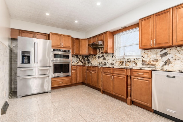 kitchen featuring light stone countertops, appliances with stainless steel finishes, backsplash, and sink