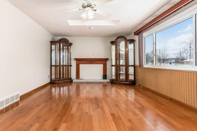 unfurnished living room with light hardwood / wood-style flooring, wooden walls, a skylight, a high end fireplace, and ceiling fan